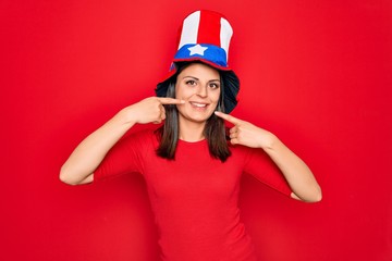 Young beautiful brunette woman wearing united states hat celebrating independence day smiling cheerful showing and pointing with fingers teeth and mouth. Dental health concept.