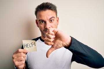 Young handsome man stressed holding reminder paper with help message with angry face, negative sign...