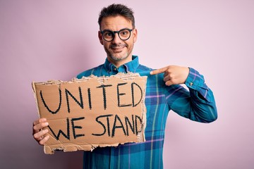 Young handsome activist man asking for union holding banner with united stand message with surprise...