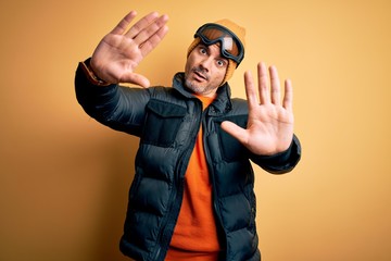 Young handsome skier man skiing wearing snow sportswear using ski goggles doing frame using hands palms and fingers, camera perspective