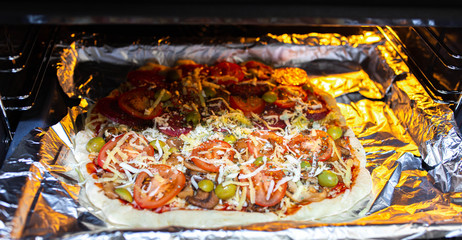 pizza with tomatoes olives, cheese and mushrooms on a foil before baking in the oven.