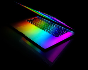 Open laptop isolated on black background with rainbow colors reflecting on keyboard