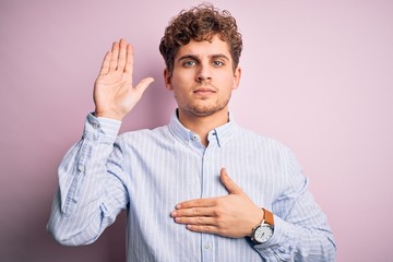 Young blond handsome man with curly hair wearing striped shirt over white background Swearing with...