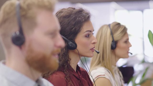 Portrait of confident woman working in a call center while looking at camera. Customer care rappresentative working with team in modern office sitting in a row. Support online with call center agent.