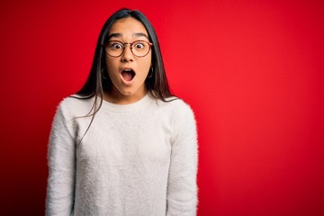 Fototapeta premium Young beautiful asian woman wearing casual sweater and glasses over red background afraid and shocked with surprise and amazed expression, fear and excited face.