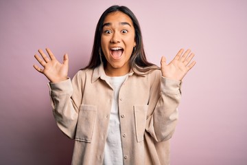 Young beautiful asian woman wearing casual shirt standing over pink background celebrating crazy and amazed for success with arms raised and open eyes screaming excited. Winner concept