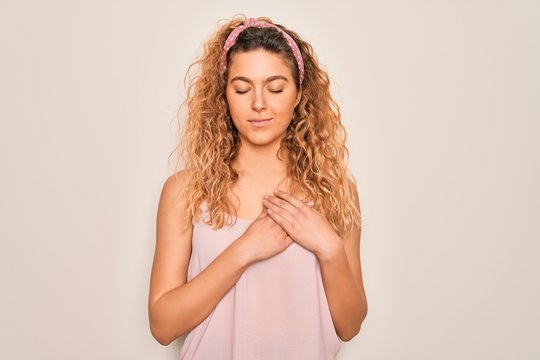 Young beautiful woman with blue eyes wearing casual t-shirt and diadem over pink background smiling with hands on chest with closed eyes and grateful gesture on face. Health concept.