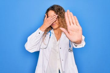 Young beautiful blonde doctor woman with blue eyes wearing coat and stethoscope covering eyes with hands and doing stop gesture with sad and fear expression. Embarrassed and negative concept.