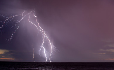 Naklejka na ściany i meble Lightning storm over the ocean at sunset