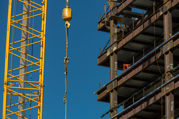 Close up of commercial office building under construction with construction workers ,steel beams with weight of steel beams sprypainted on the beams. The scene is against a blue sky