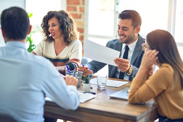 Group of business workers smiling happy working together. Sitting on desk with smile on face reading documents at the office