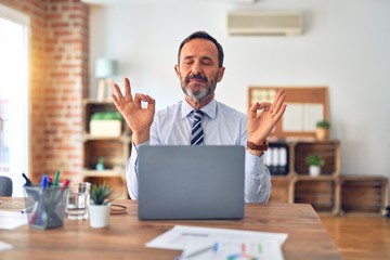 Middle age handsome businessman wearing tie sitting using laptop at the office relax and smiling with eyes closed doing meditation gesture with fingers. Yoga concept.