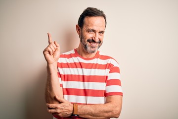 Middle age hoary man wearing casual striped t-shirt standing over isolated white background with a big smile on face, pointing with hand and finger to the side looking at the camera.
