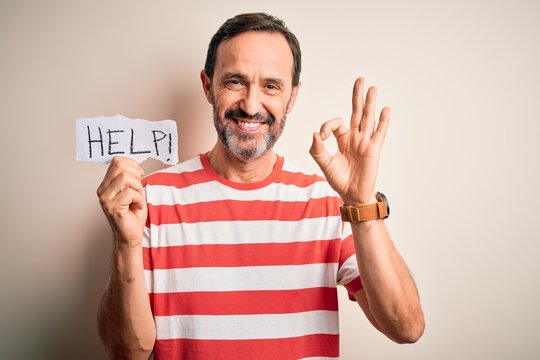 Middle age hoary man holding paper with help message over isolated white background doing ok sign with fingers, excellent symbol