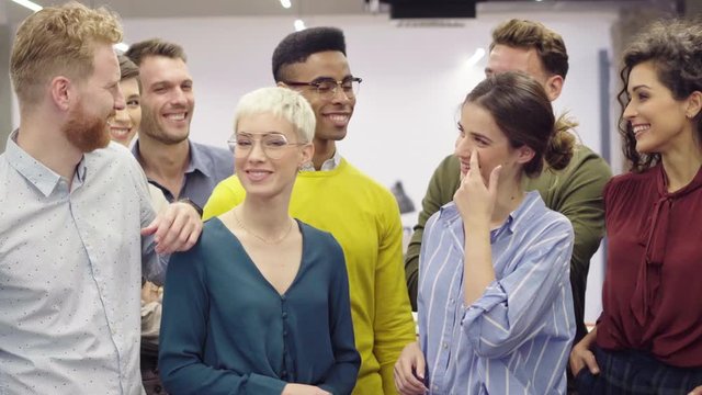 Successful creative group of casual business people talking to each other in modern office. Happy multiethnic business partners standing as a team and laughing together in co-working space.
