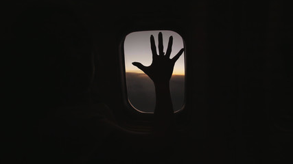 The silhouette of a female hand is moving along the airplane window.