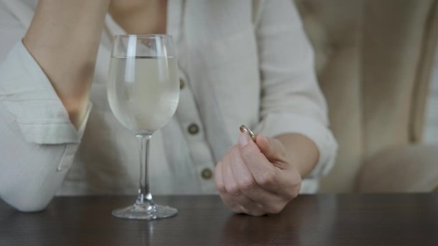 Divorce. A woman with a glass of wine is going through a divorce, holding a wedding ring in her hand.