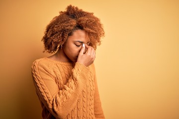 Young beautiful African American afro woman with curly hair wearing casual sweater tired rubbing nose and eyes feeling fatigue and headache. Stress and frustration concept.