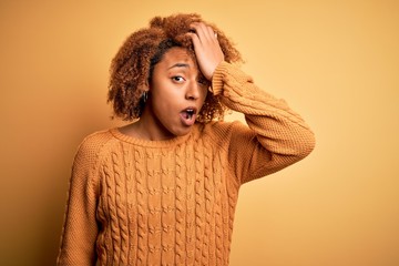 Young beautiful African American afro woman with curly hair wearing casual sweater surprised with...