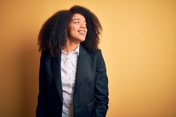 Young beautiful african american business woman with afro hair wearing elegant jacket looking away to side with smile on face, natural expression. Laughing confident.