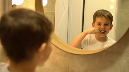 Little boy brushing his teeth in bathroom in front of mirror, oral hygiene