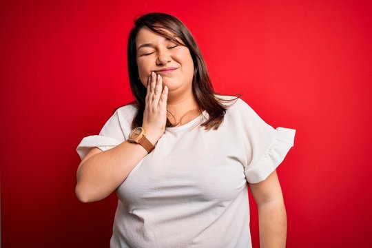 Beautiful brunette plus size woman wearing casual t-shirt over isolated red background touching mouth with hand with painful expression because of toothache or dental illness on teeth. Dentist
