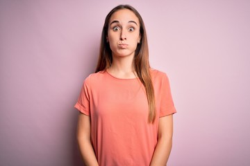 Fototapeta premium Young beautiful woman wearing casual t-shirt standing over isolated pink background puffing cheeks with funny face. Mouth inflated with air, crazy expression.
