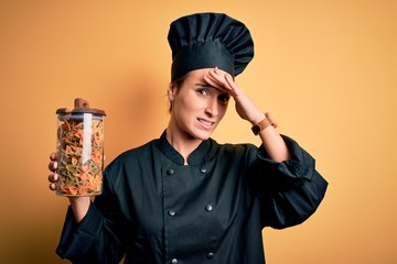 Young beautiful chef woman wearing cooker uniform and hat holding bottle with italian pasta...