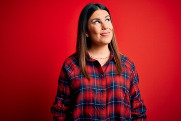 Fototapeta premium Young beautiful woman wearing casual shirt over red background smiling looking to the side and staring away thinking.