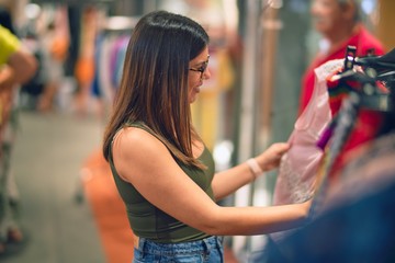 Young beautiful woman smiling happy and confident. Standing with smile on face looking clothes at store