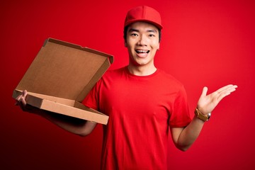 Young handsome chinese delivery man holding deliver box with delicious Italian pizza very happy and excited, winner expression celebrating victory screaming with big smile and raised hands