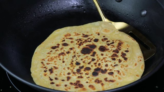 Cooking Indian grated Cauliflower stuffed flatbread Paratha on a skillet.