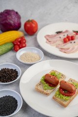 Sausage with tomatoes, salad and two sets of bread on a white plate.