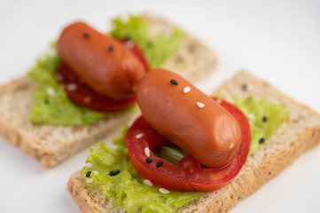 Sausage with tomatoes, salad and two sets of bread on a white plate.