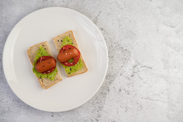 Sausage with tomatoes, salad and two sets of bread on a white plate.