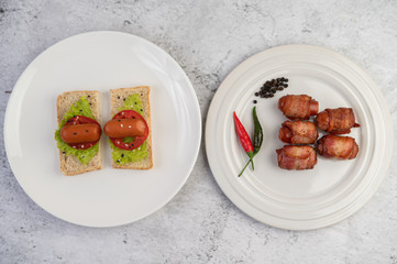Sausage wrapped pork belly on a white plate and sausage put on bread.