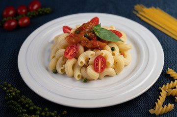 Stir-fried macaroni with tomato, chili, pepper seeds and basil in a white dish.