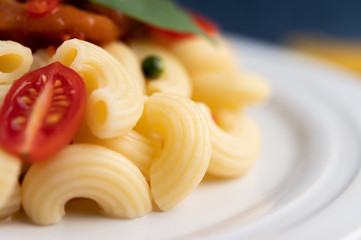 Stir-fried macaroni with tomato, chili, pepper seeds and basil in a white dish.