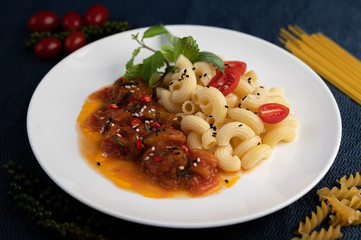 Stir-fried macaroni with tomato, chili, pepper seeds and basil in a white dish.
