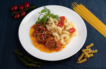 Stir-fried macaroni with tomato, chili, pepper seeds and basil in a white dish.