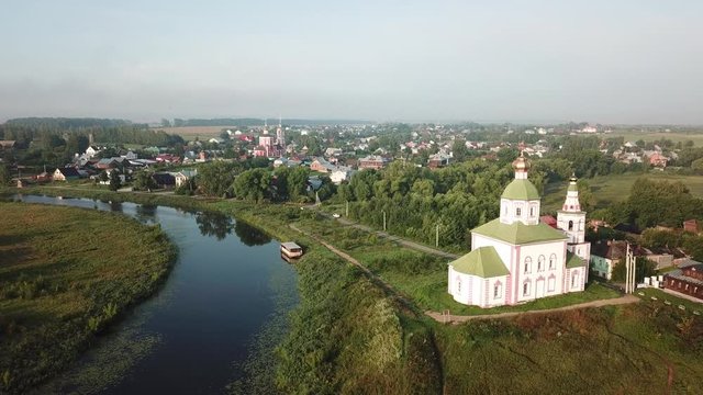 4K aerial dense sunny summer morning video of Suzdal churches, buildings, hills, fields and cathedrals located on Kamenka River shore in Vladimir Region, Russia