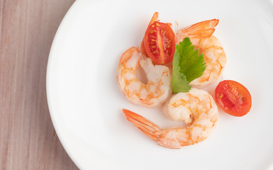 Three fresh shrimp and half tomatoes in a white plate on a wooden.