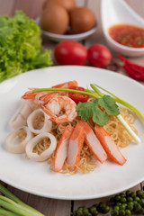 Stir-fried instant noodle with prawn and crab stick along  in a white dish.