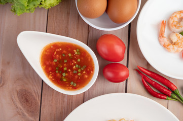 Three fresh shrimp, eggs, chili, sauce and half tomatoes in a white plate on a wooden.