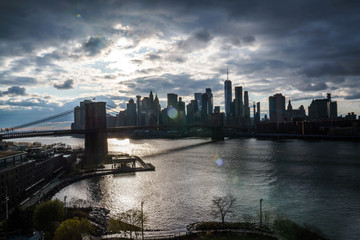 Manhattan skyline with Brooklyn bridge. Sky-rise skyscrapers tall apartment buildings. Dramatic cloudy sky with sun rays. 