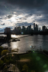 Manhattan skyline with Brooklyn bridge. Sky-rise skyscrapers tall apartment buildings. Dramatic cloudy sky with sun rays. 