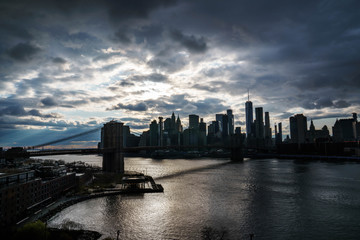 Manhattan skyline with Brooklyn bridge. Sky-rise skyscrapers tall apartment buildings. Dramatic cloudy sky with sun rays. 