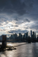 Manhattan skyline with Brooklyn bridge. Sky-rise skyscrapers tall apartment buildings. Dramatic cloudy sky with sun rays. 