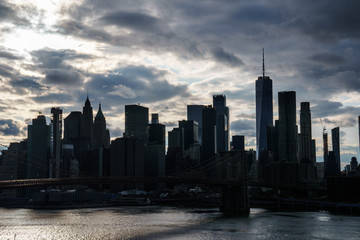 Manhattan skyline with Brooklyn bridge. Sky-rise skyscrapers tall apartment buildings. Dramatic cloudy sky with sun rays. 