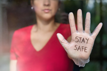 woman wearing sanitary glove that says "stay safe" through the window. Close up